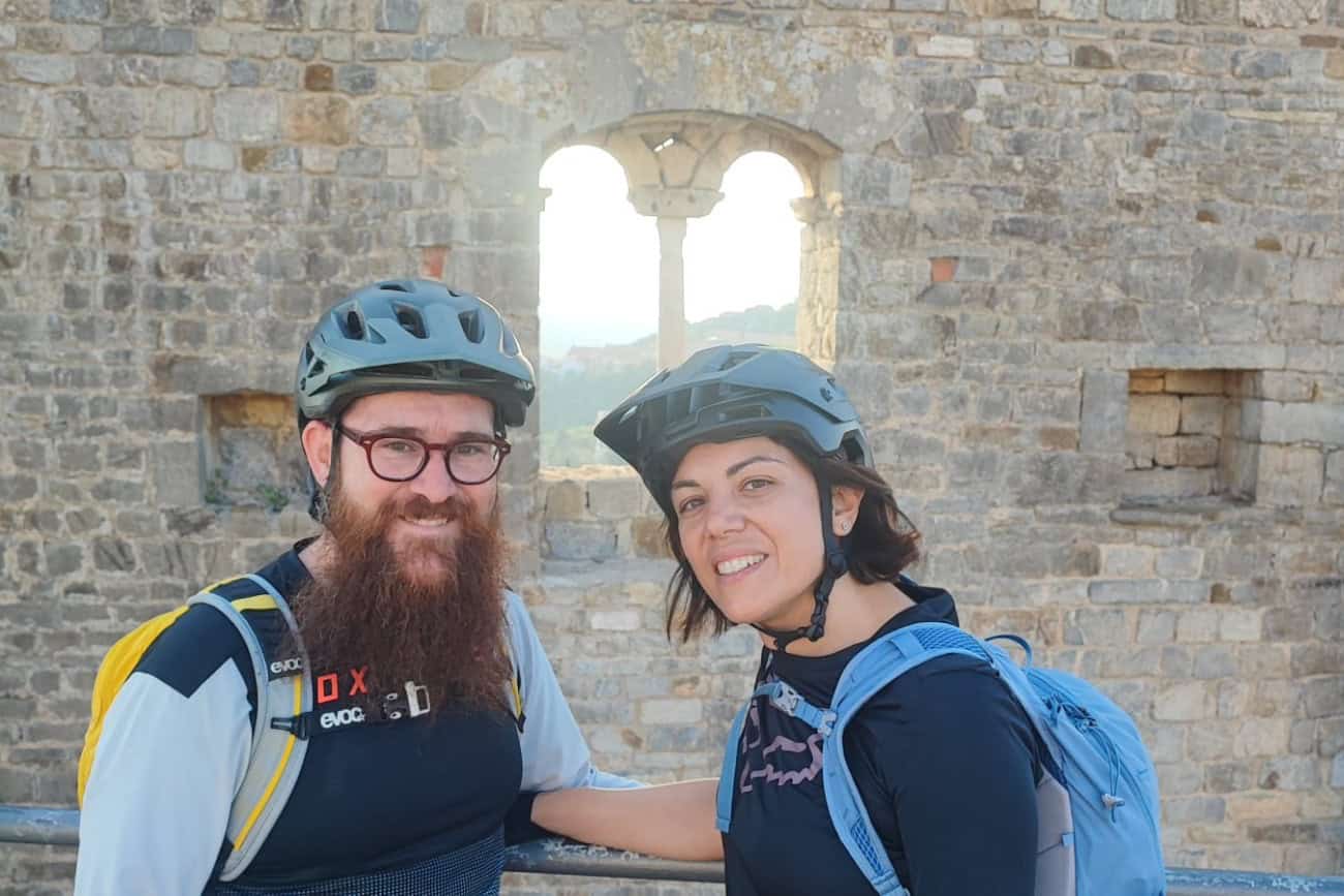 Coppia di ciclisti sorridenti davanti a una finestra bifora della Rocca di Campiglia Marittima