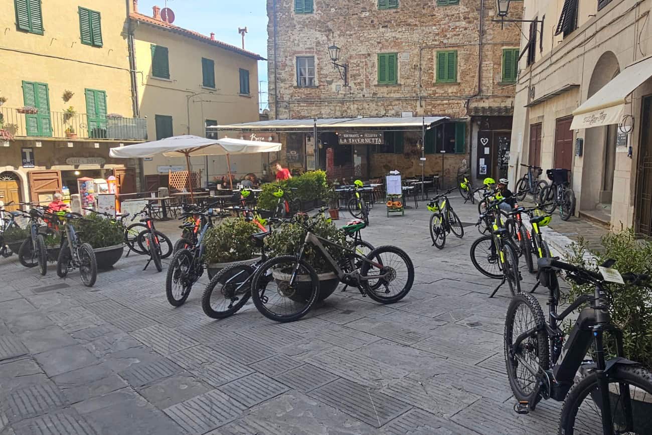 E-bike parcheggiate nella piazza principale del centro storico di Campiglia marittima, circondate da edifici medievali