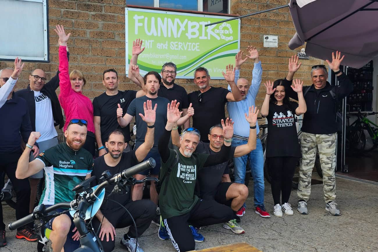 Gruppo di partecipanti sorride davanti all'insegna di Funnybike, pronti per un'avventura in e-bike tra Campiglia e Suvereto