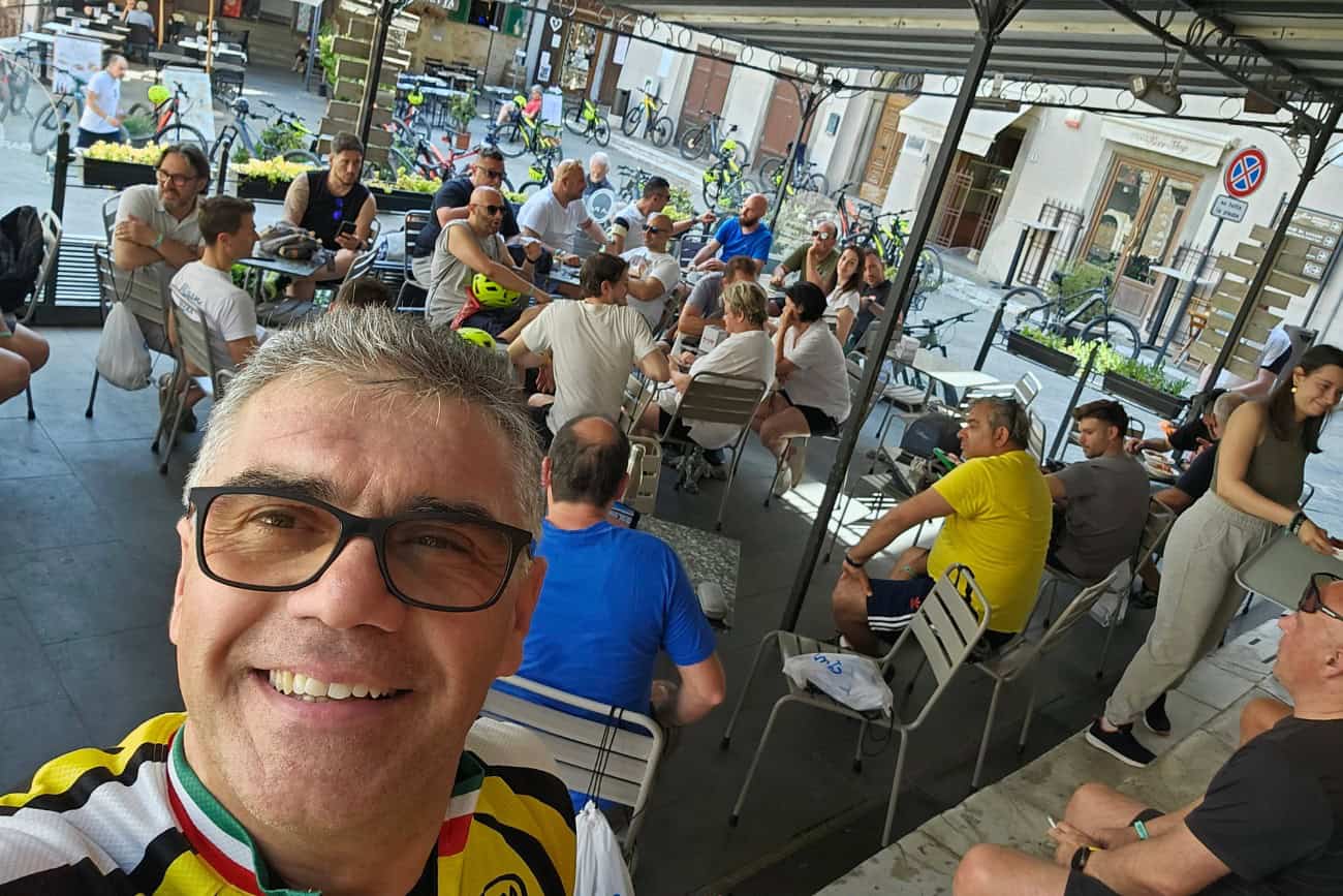 Stefano Barbieri con gruppo di ciclisti che si rilassa in un bar all'aperto nella piazza di Campiglia Marittima dopo l'escursione in e-bike