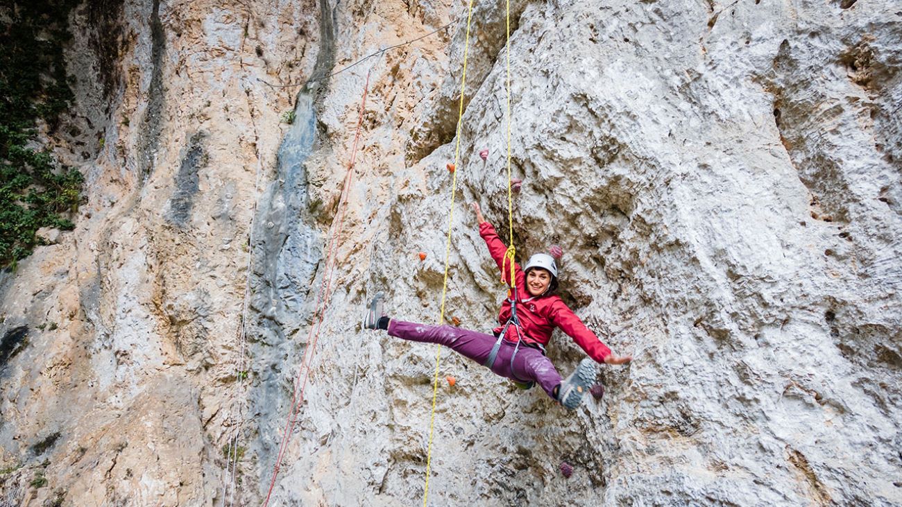 Ragazza che si arrampica sulla falesia alle grotte di equi, assicurata alle funi