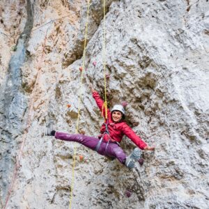 Donna assicurata alle funi che si arrampica alla falesia delle grotte di equi
