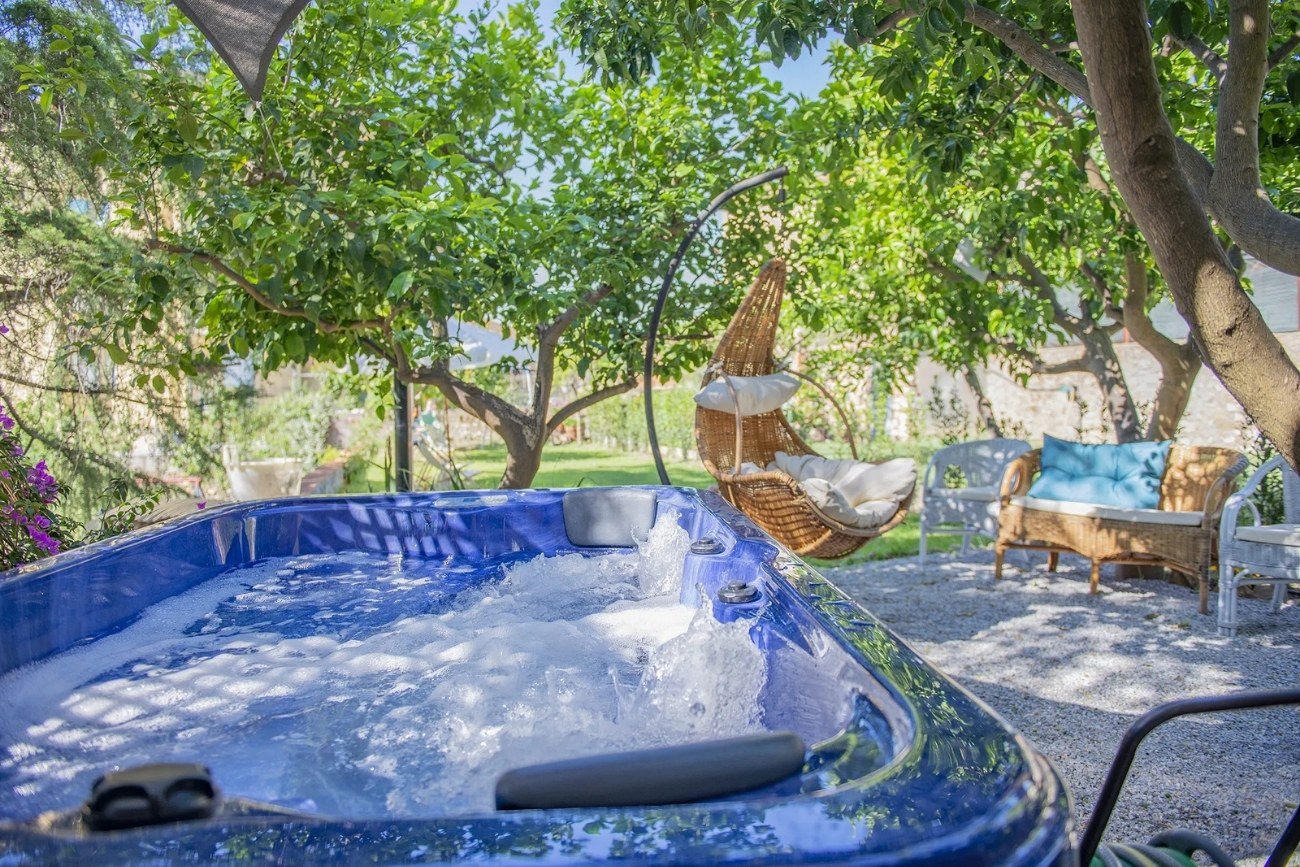 Jacuzzi esterna immersa nel giardino del B&B Il Giardino dei Limoni a Suvereto, circondata da alberi di limone, sedute in rattan e una poltrona sospesa